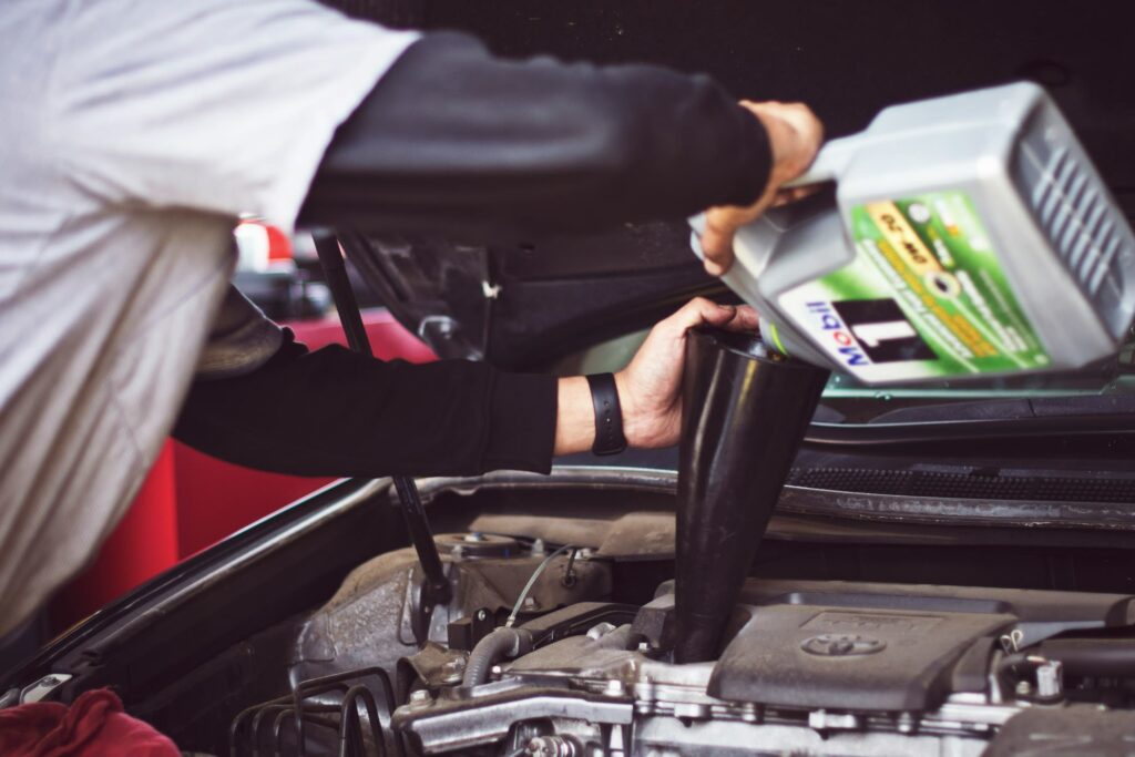 Technician filling a car with oil in a shop, while using a funnel